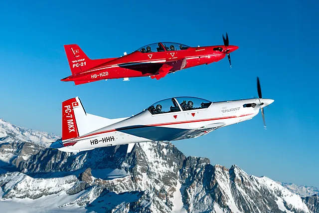 Two Pilatus trainers flying in close formation above mountain terrain.